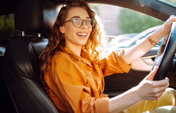 Image of a Caucasian woman in an orange shirt behind the wheel of a car.