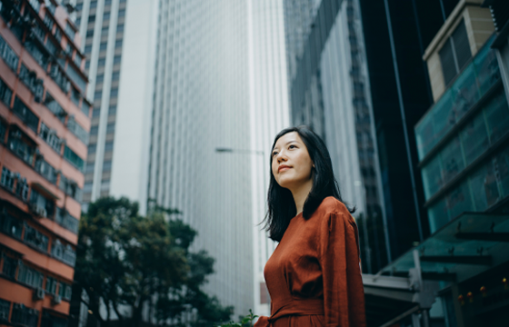 A young Asian woman wearing an orange blouse looking up in the city